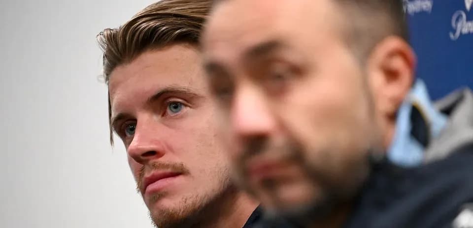 Two individuals at a press conference, one in focus