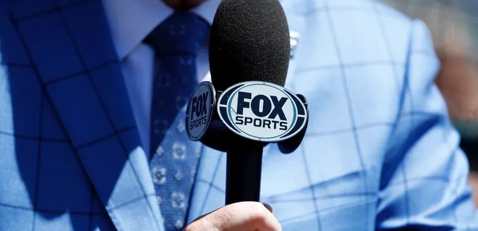 Person holding FOX Sports microphone in blue suit