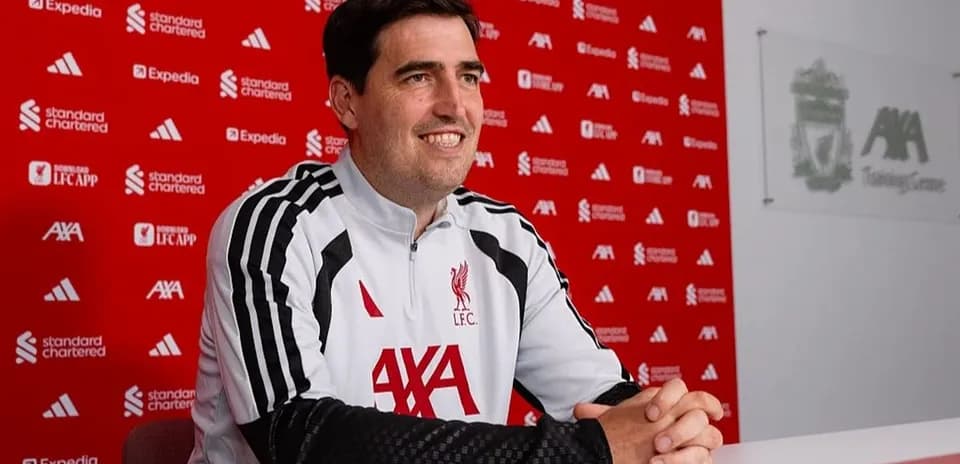 Coach seated at press conference table with Liverpool branding