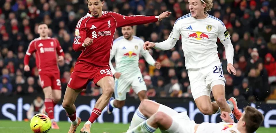 Liverpool player dribbling past Leeds defenders on pitch