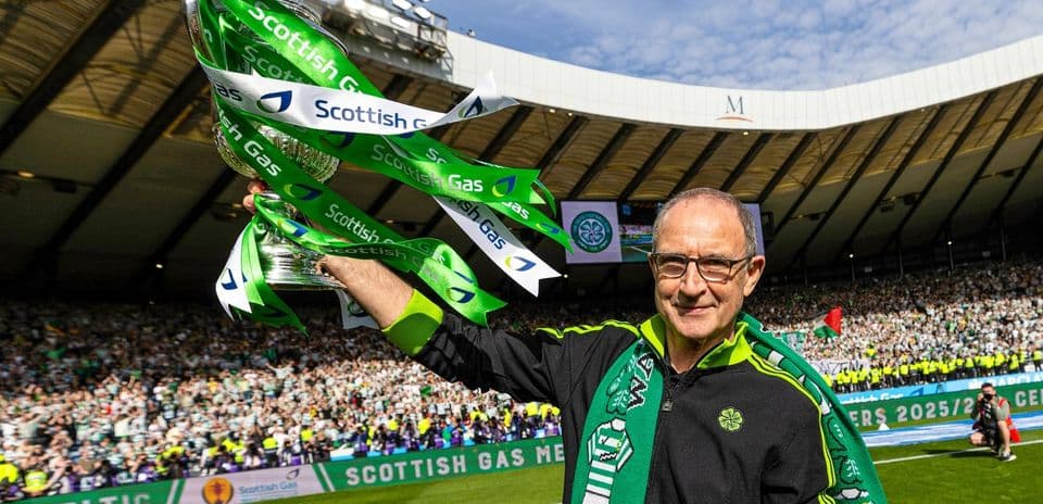Man holding trophy with Celtic supporters in background