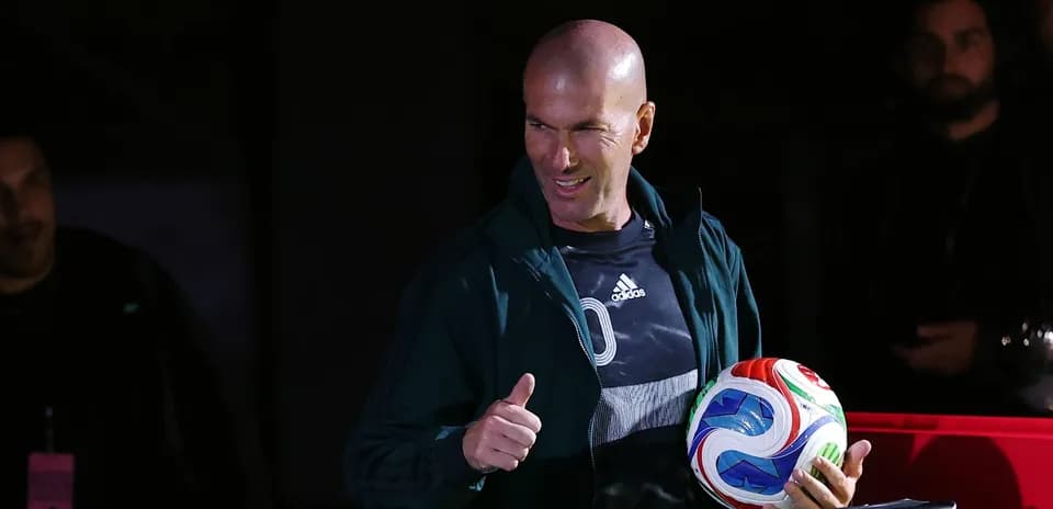 Zinedine Zidane holding a soccer ball and giving thumbs up