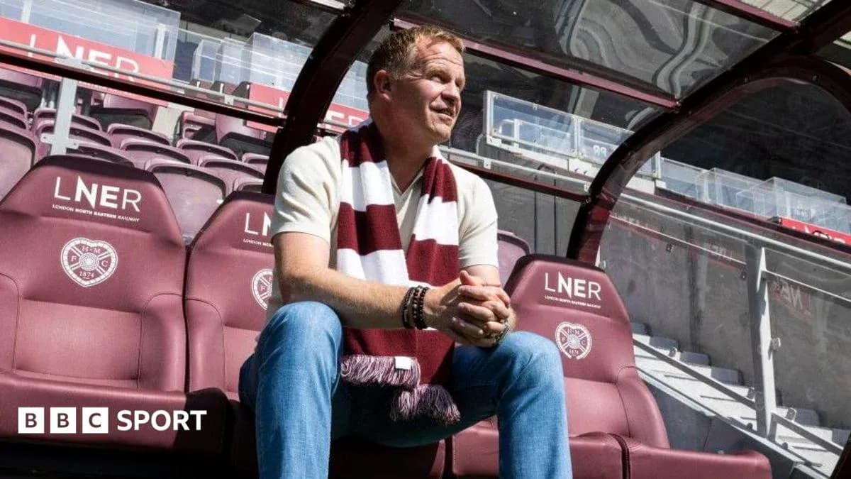 Manager seated in stadium dugout wearing team scarf