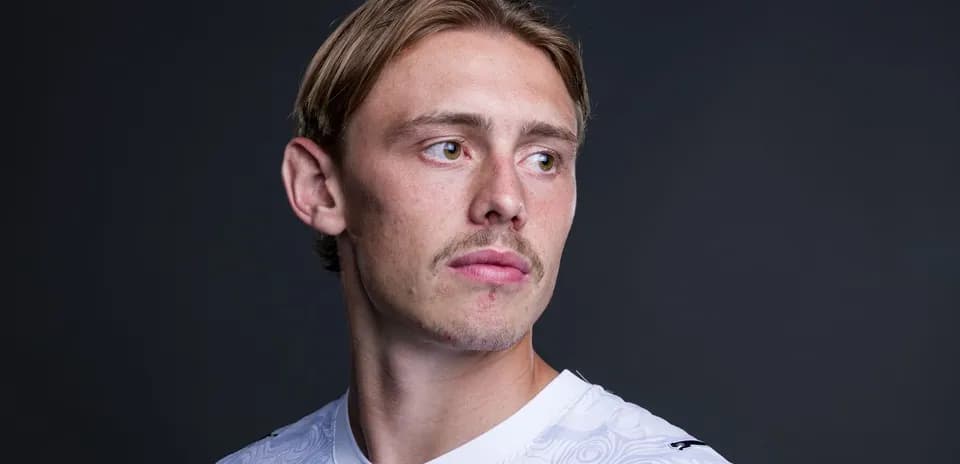 Athlete posing in white sports jersey against dark background