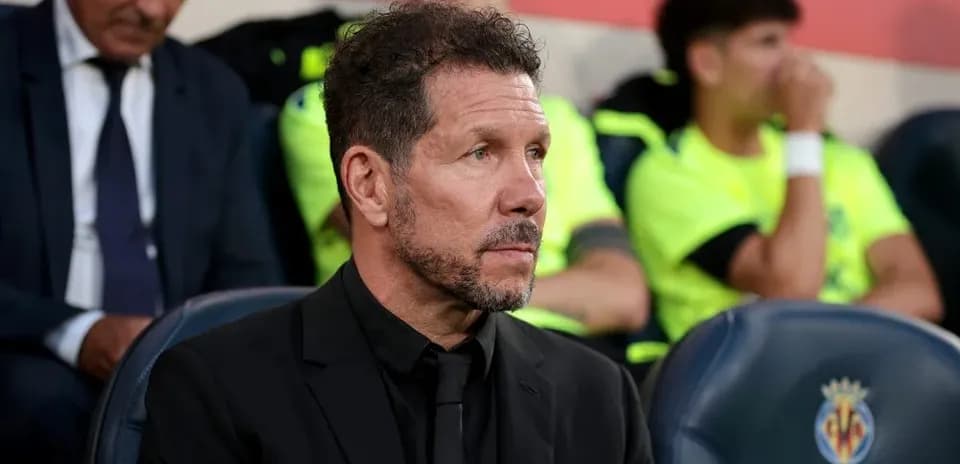Coach seated on bench during match, players in background