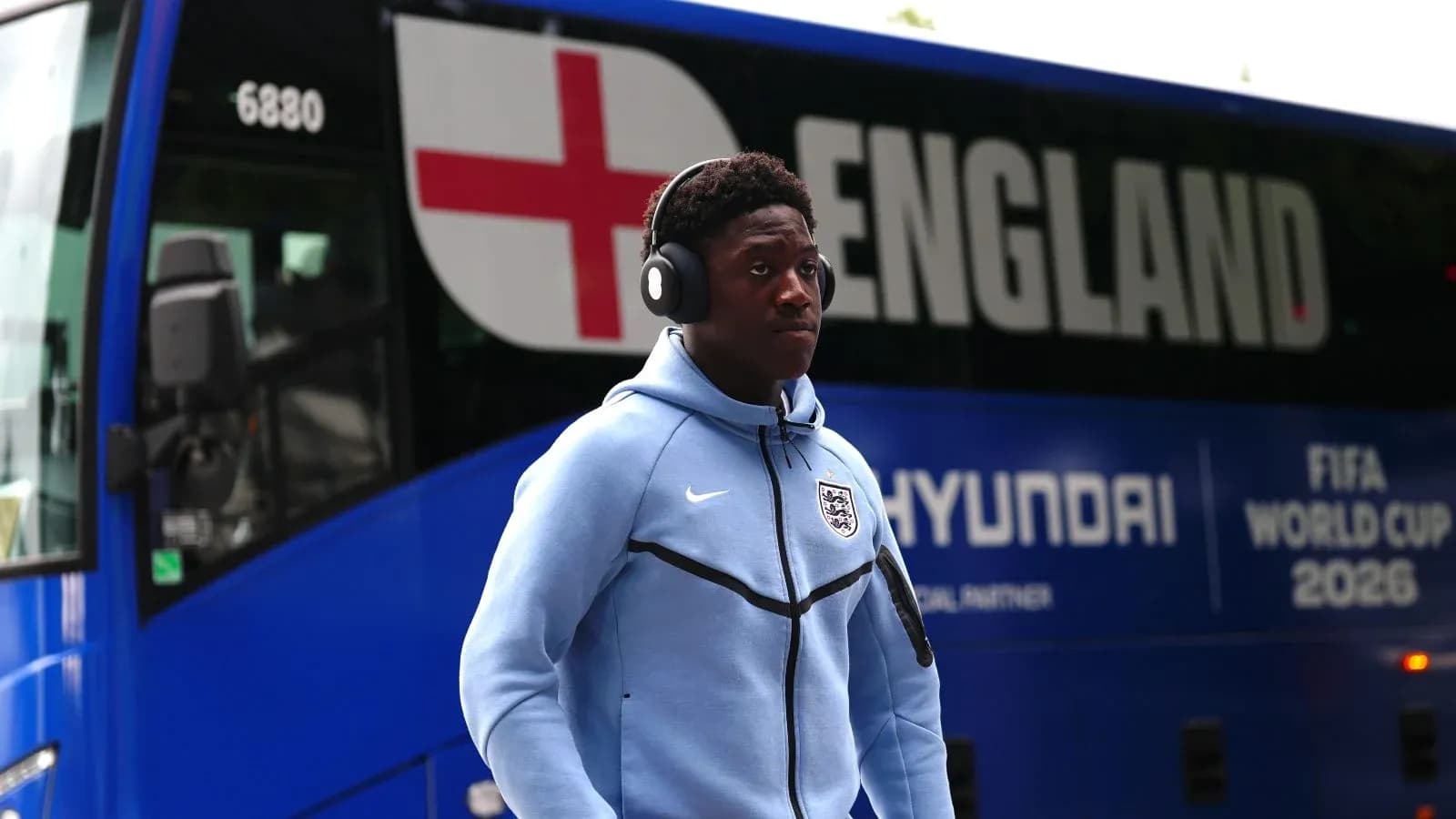 Player wearing headphones near England team bus