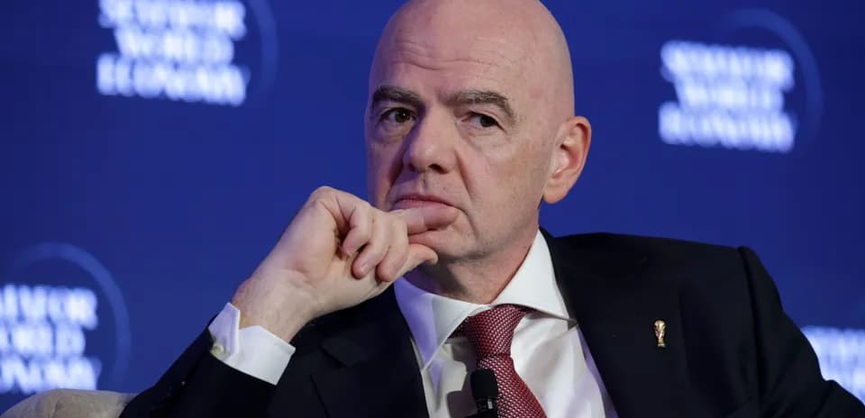 Man in suit speaking at conference with FIFA emblem