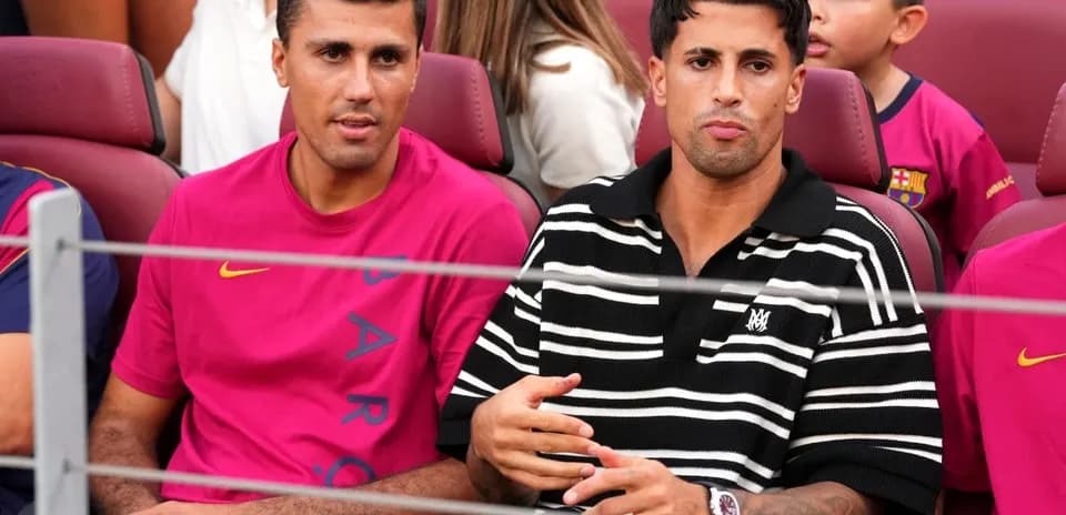 Two men seated in stadium, wearing team jerseys