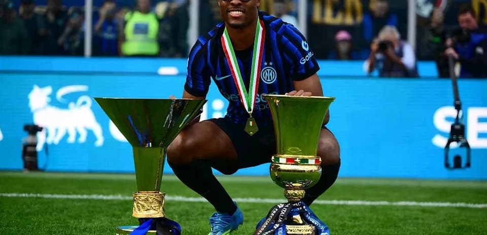 Player celebrating with two trophies on the pitch