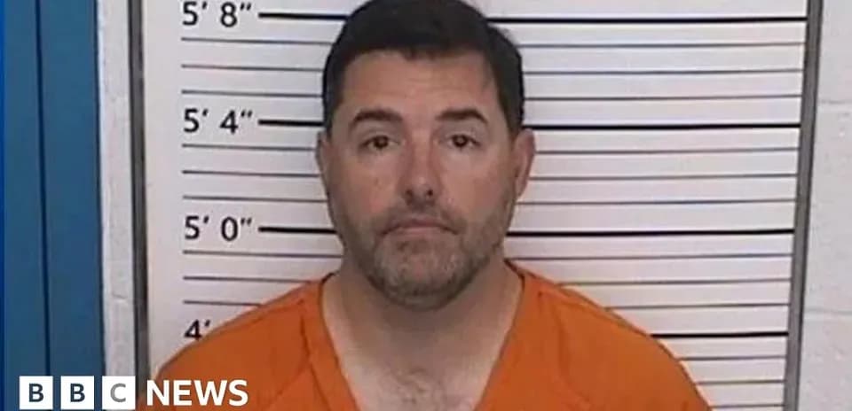 Man in orange jumpsuit at police mugshot backdrop