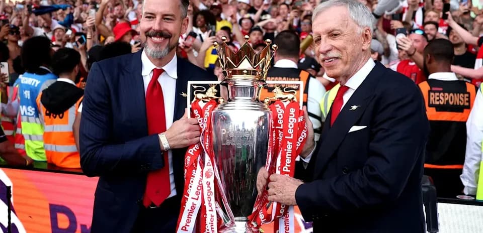 Two officials holding Premier League trophy with fans cheering