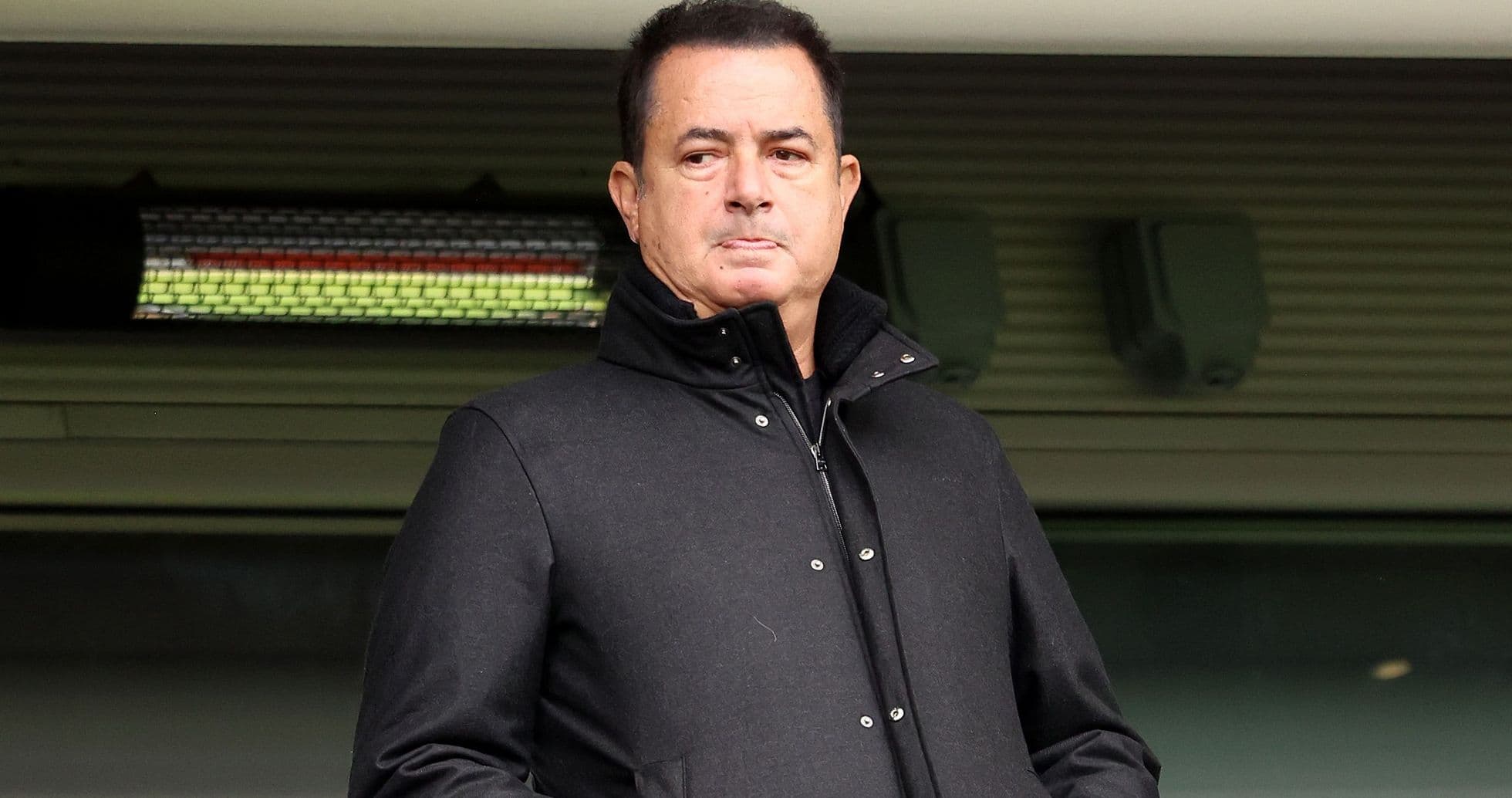 Man standing in a stadium wearing a black coat