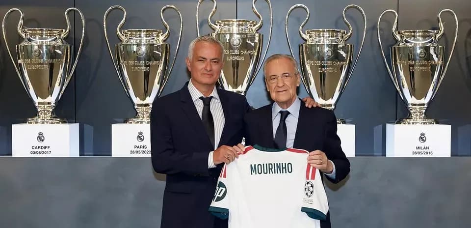 Two men holding a jersey in front of trophies