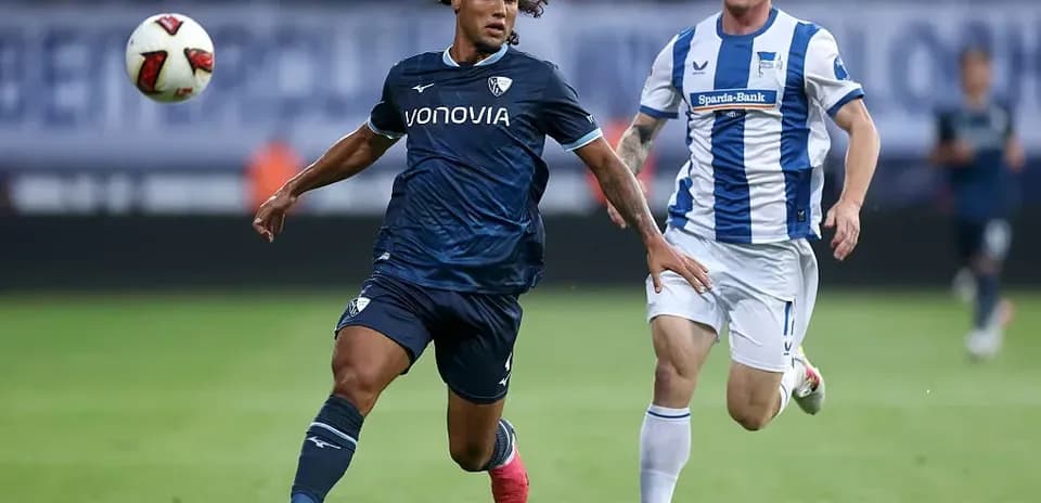 Player in dark kit dribbling past opponent in light kit