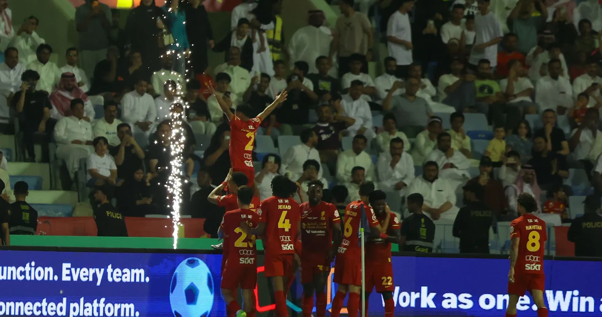 Players celebrating a goal with fireworks in background