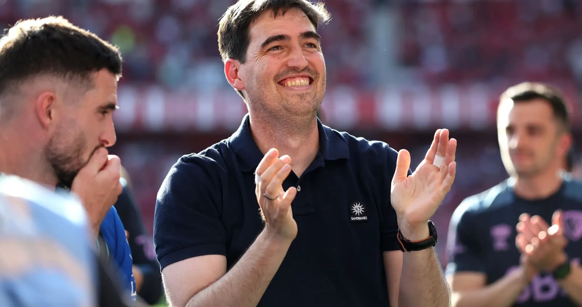 Man in polo shirt clapping with players nearby