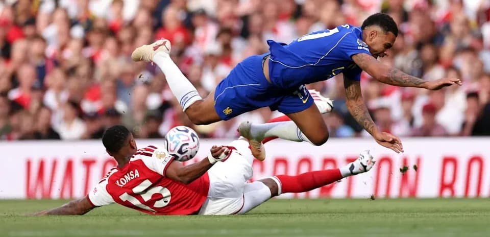 Player from Chelsea jumping over fallen Arsenal player