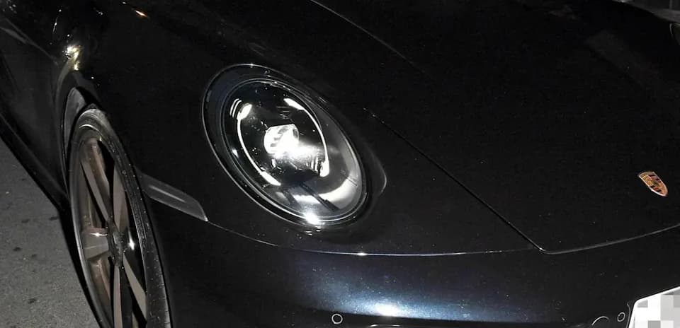 Two men inside a black Porsche car at night
