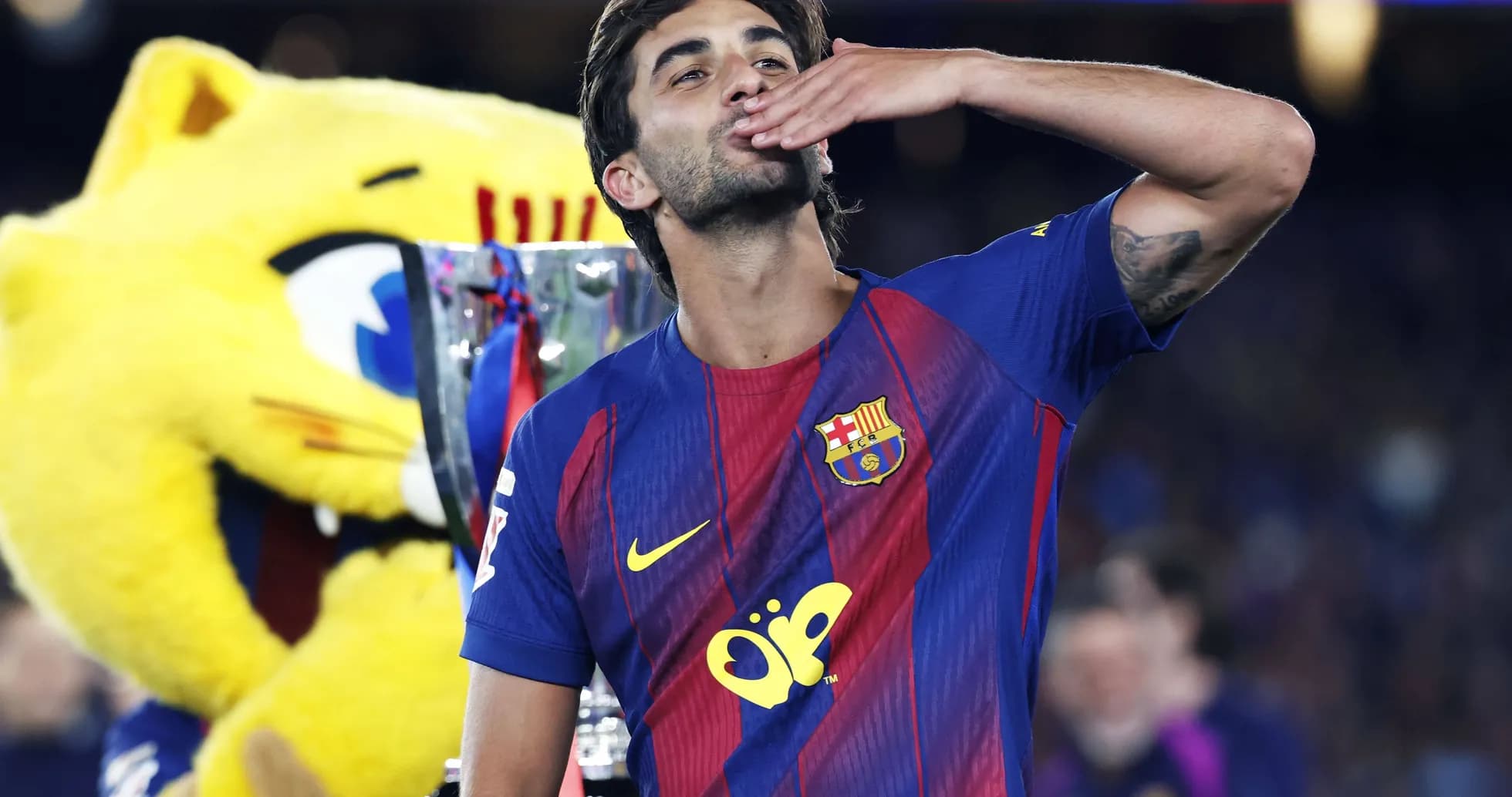 Player celebrating with trophy and mascot in background
