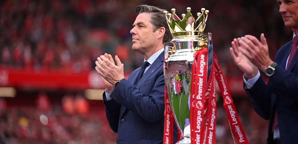 Man in suit applauding near Premier League trophy
