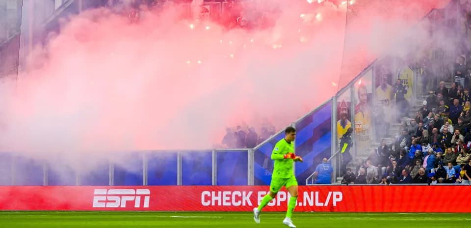 Goalkeeper walking past smoky crowd during match