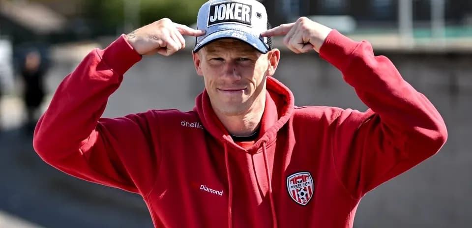 Man in red hoodie pointing at his cap
