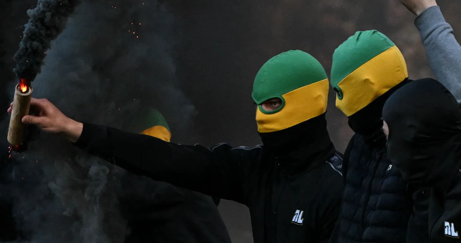 Masked individuals holding a flare amid smoke