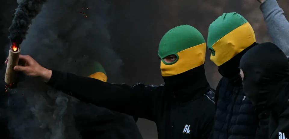 Masked individuals holding a flare amid smoke