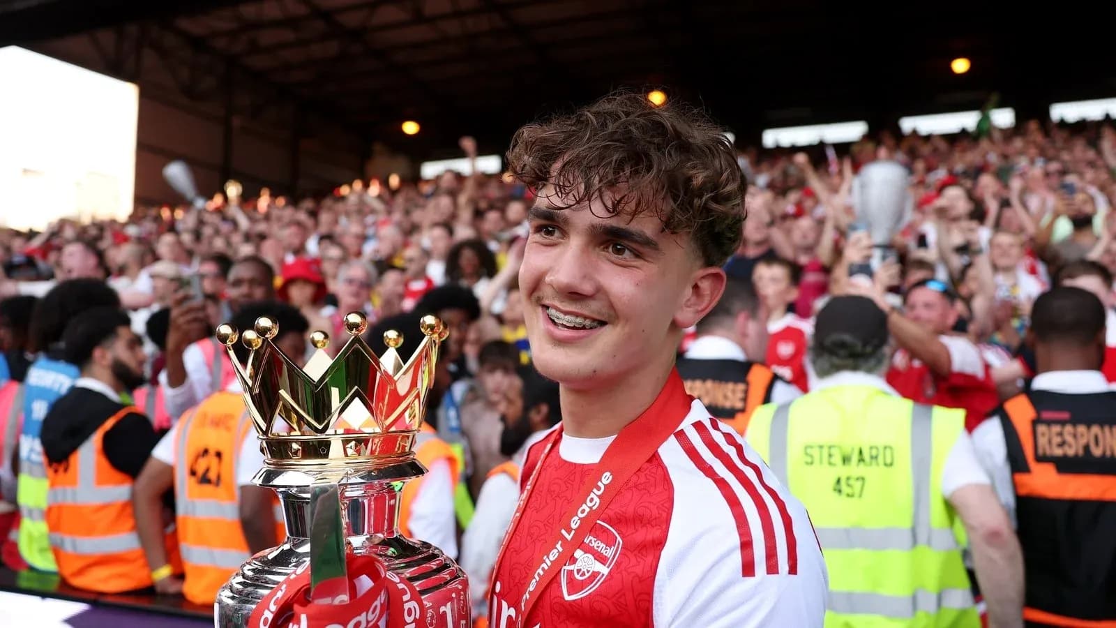 Player holding Premier League trophy with celebrating crowd