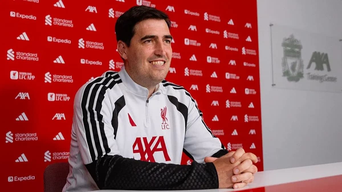 Coach seated at press conference table with Liverpool branding Coach seated at press conference table with Liverpool branding