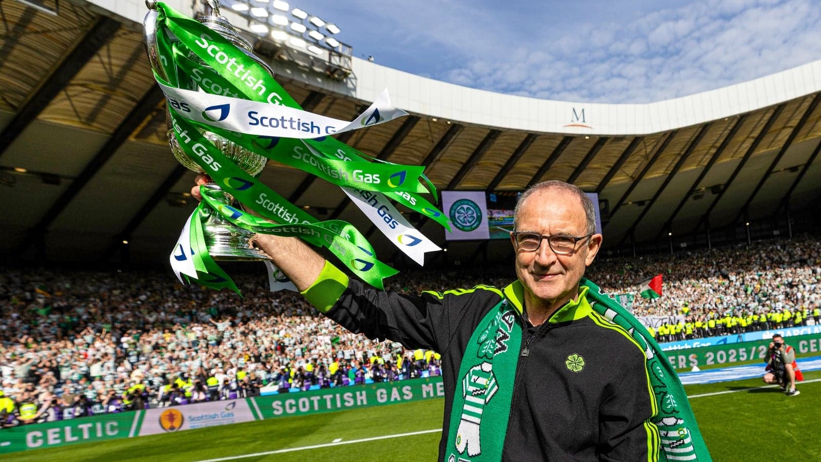 Man holding trophy with Celtic supporters in background Man holding trophy with Celtic supporters in background