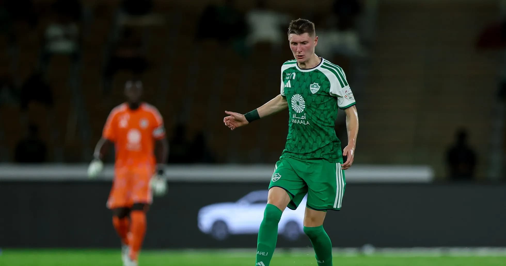 Player in green kit dribbling ball on field Player in green kit dribbling ball on field