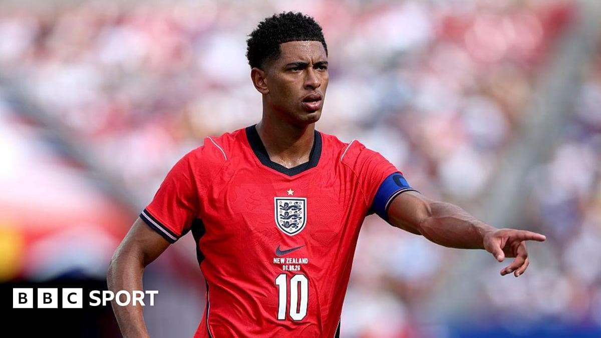 Player in red England kit directing teammates on field Player in red England kit directing teammates on field