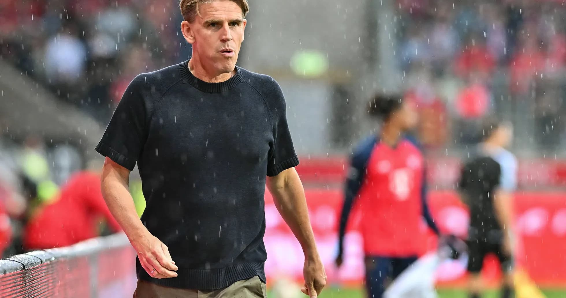 Coach walking along sideline during rainy match Coach walking along sideline during rainy match
