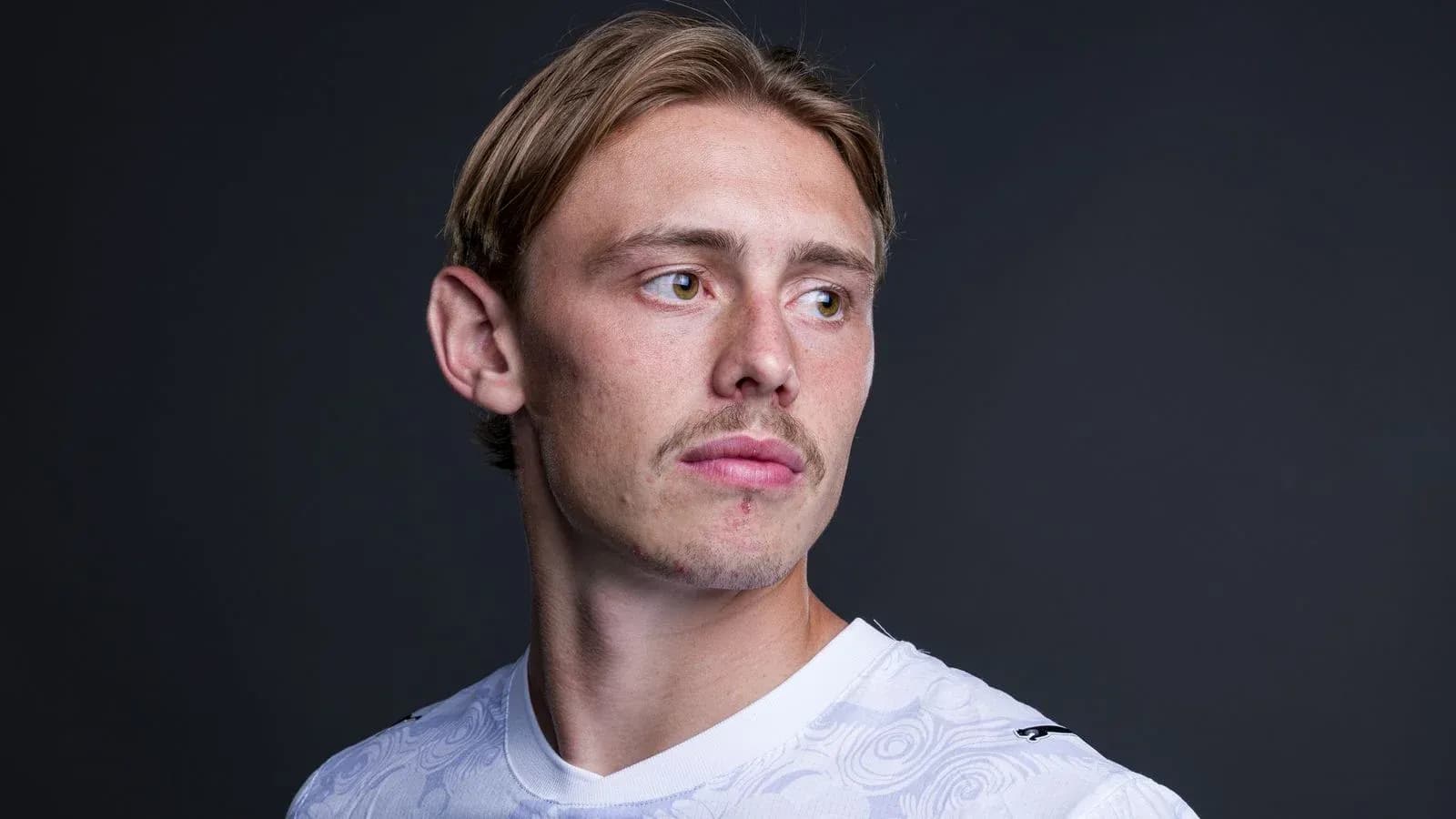 Athlete posing in white sports jersey against dark background Athlete posing in white sports jersey against dark background