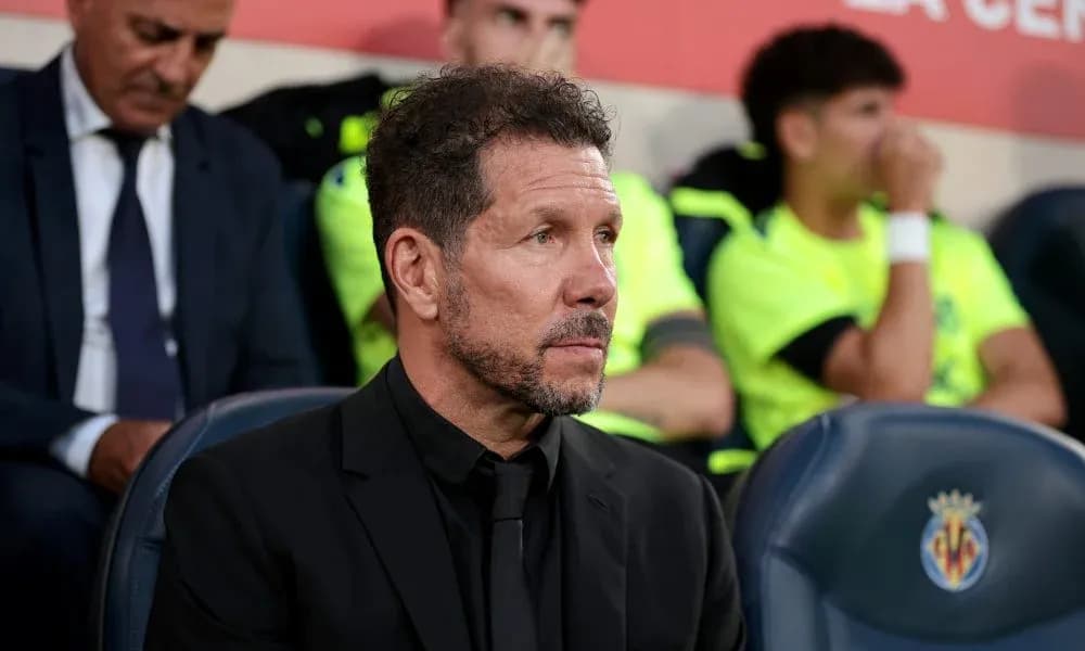 Coach seated on bench during match, players in background Coach seated on bench during match, players in background