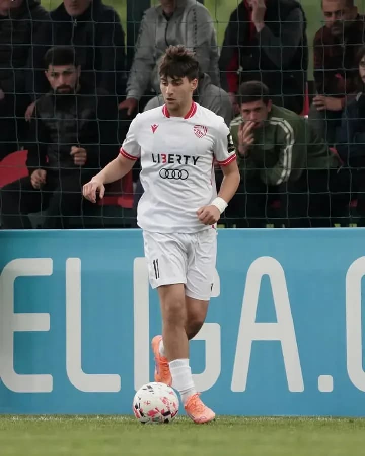 Player in white kit dribbling ball on field Player in white kit dribbling ball on field