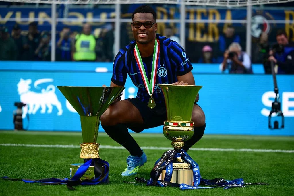 Player celebrating with two trophies on the pitch Player celebrating with two trophies on the pitch