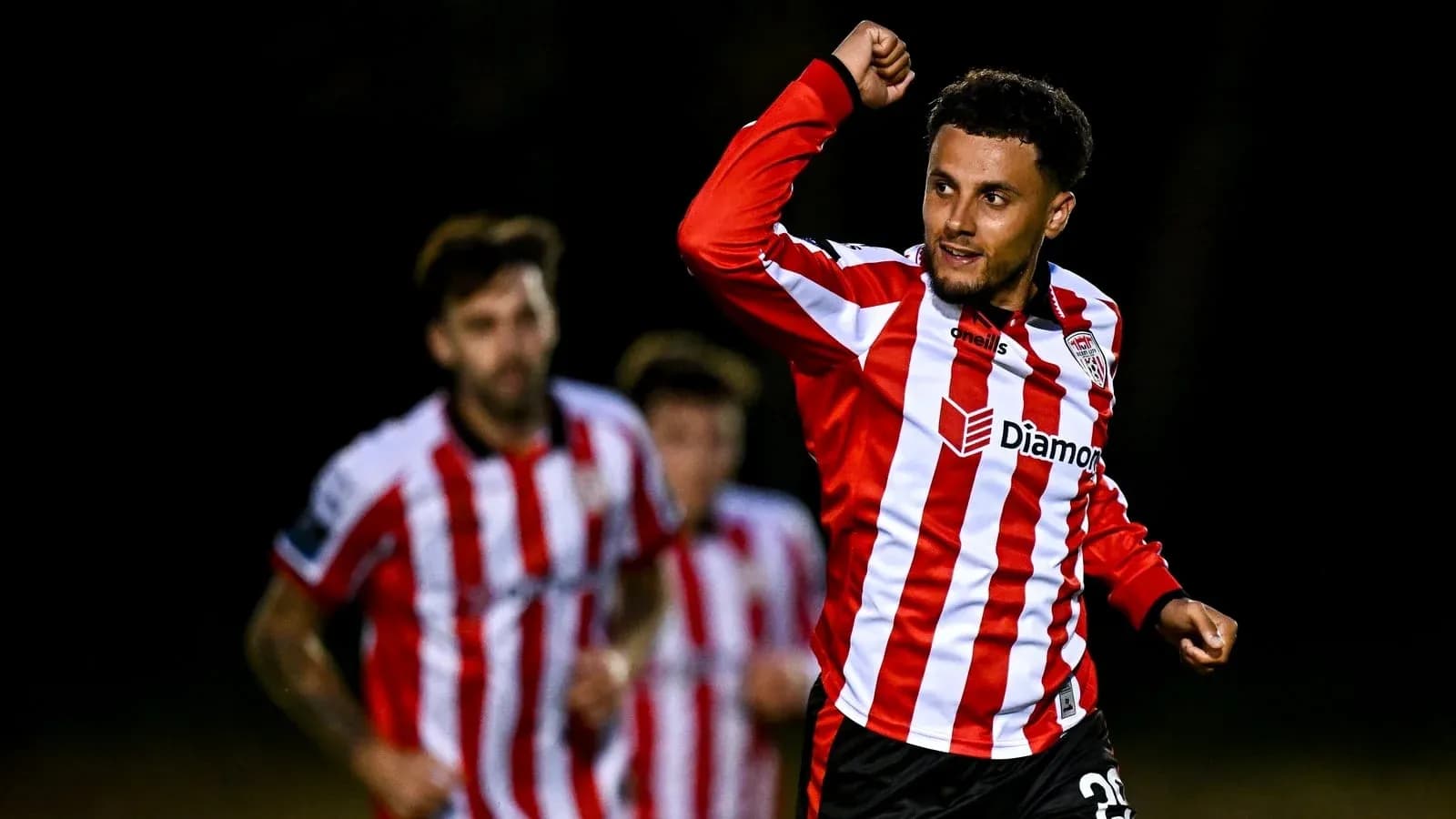 Player celebrating a goal with teammates in background Player celebrating a goal with teammates in background