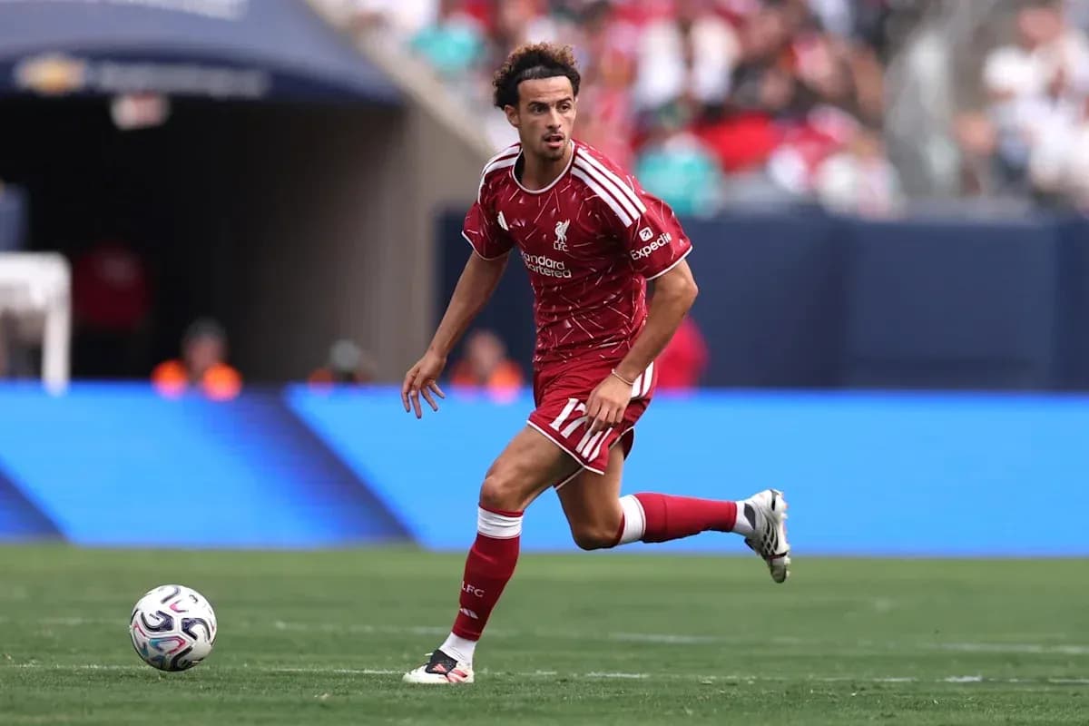 Player in red Liverpool kit dribbling ball on field Player in red Liverpool kit dribbling ball on field
